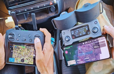 Hands holding two cameras that show images of the forest and technical information