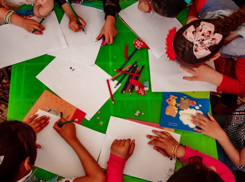 A group of children painting at a table, seen from above