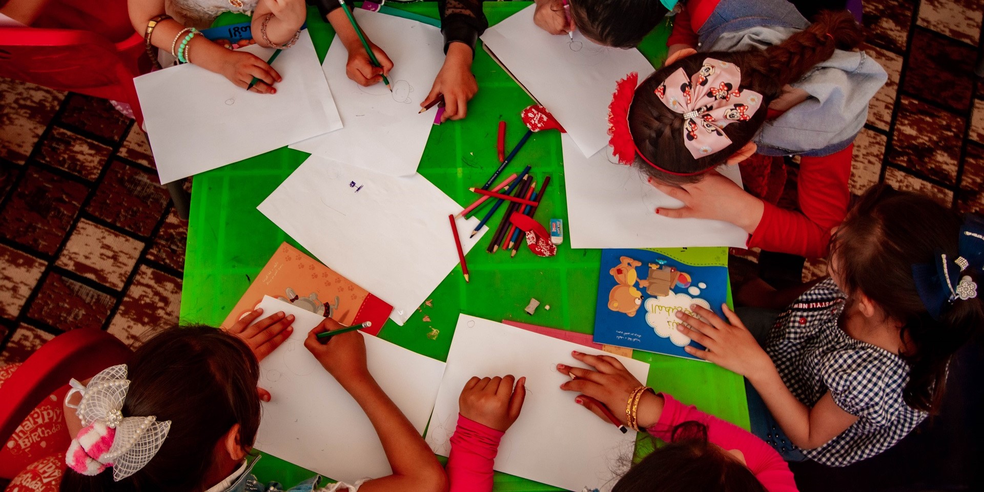 A group of children painting at a table, seen from above