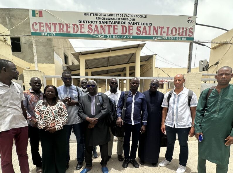 A group of 11 people stand in front of a sign that says "Health Center of Saint-Louis" in French.