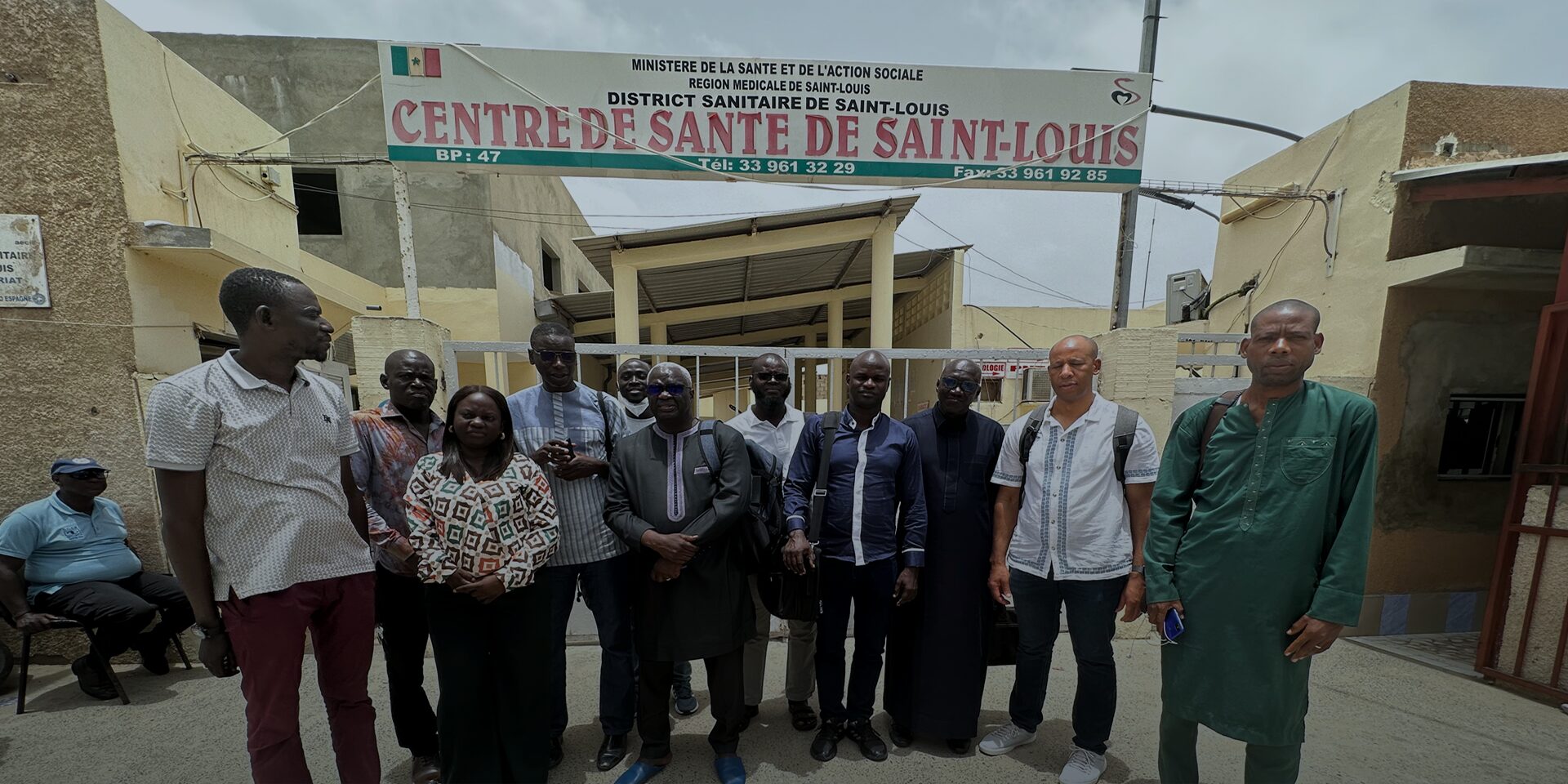 A group of 11 people stand in front of a sign that says "Health Center of Saint-Louis" in French.