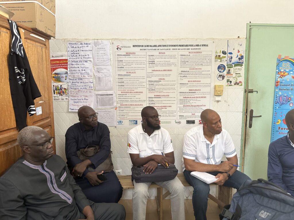 Four people sit in a circle listening to someone with posters on the wall