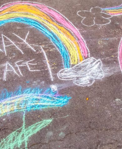 Chalk drawings of rainbows and the words stay safe on a pavement