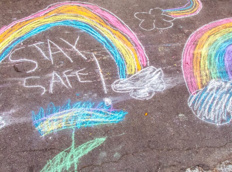 Chalk drawings of rainbows and the words stay safe on a pavement