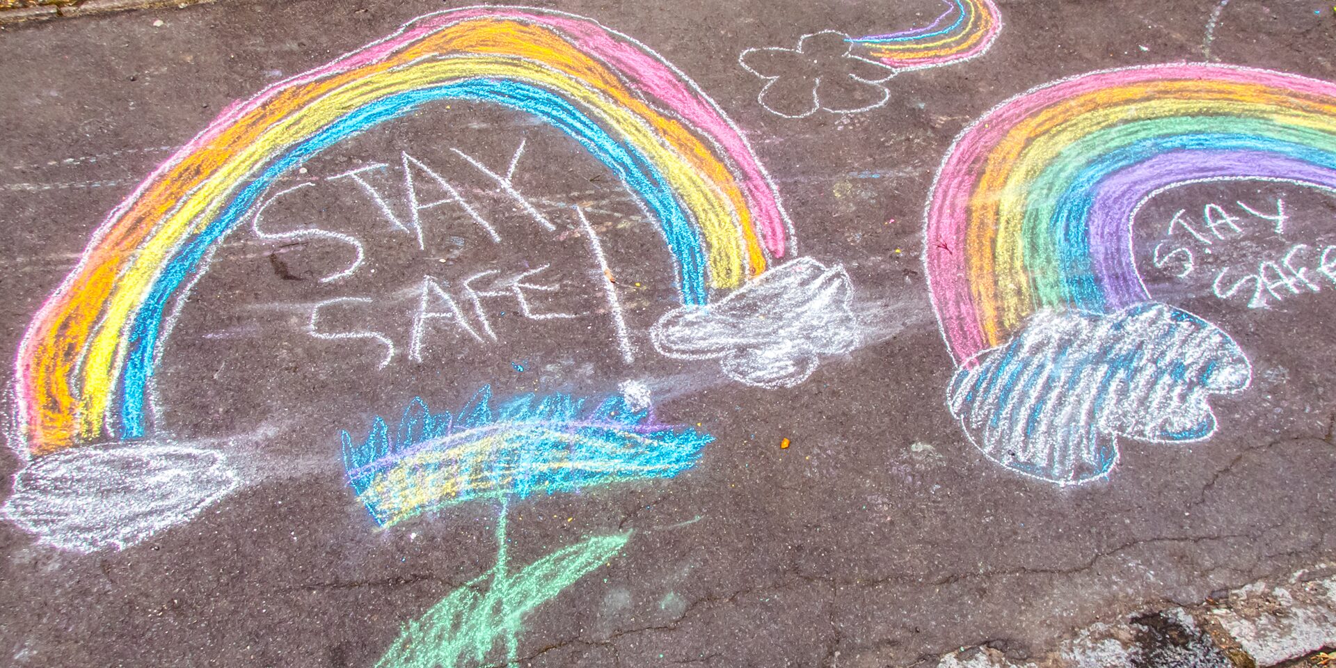 Chalk drawings of rainbows and the words stay safe on a pavement