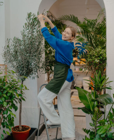 A woman on a small stepladder tends to plants in a shop